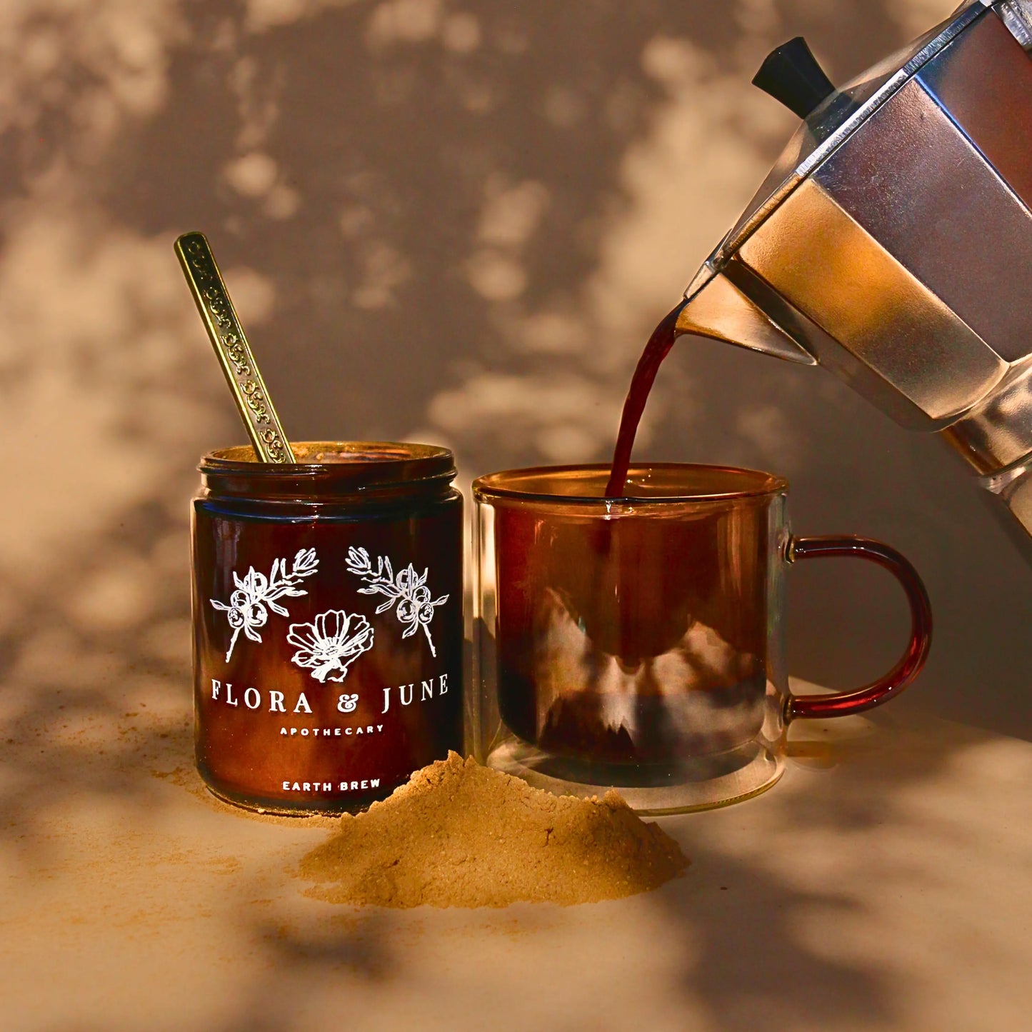A soothing pour combining fresh coffee with Flora & June's Earth Brew into a clear mug beside its amber jar, with scattered herbal powder on a surface bathed in sunlight, capturing the essence of a healthful coffee substitute.