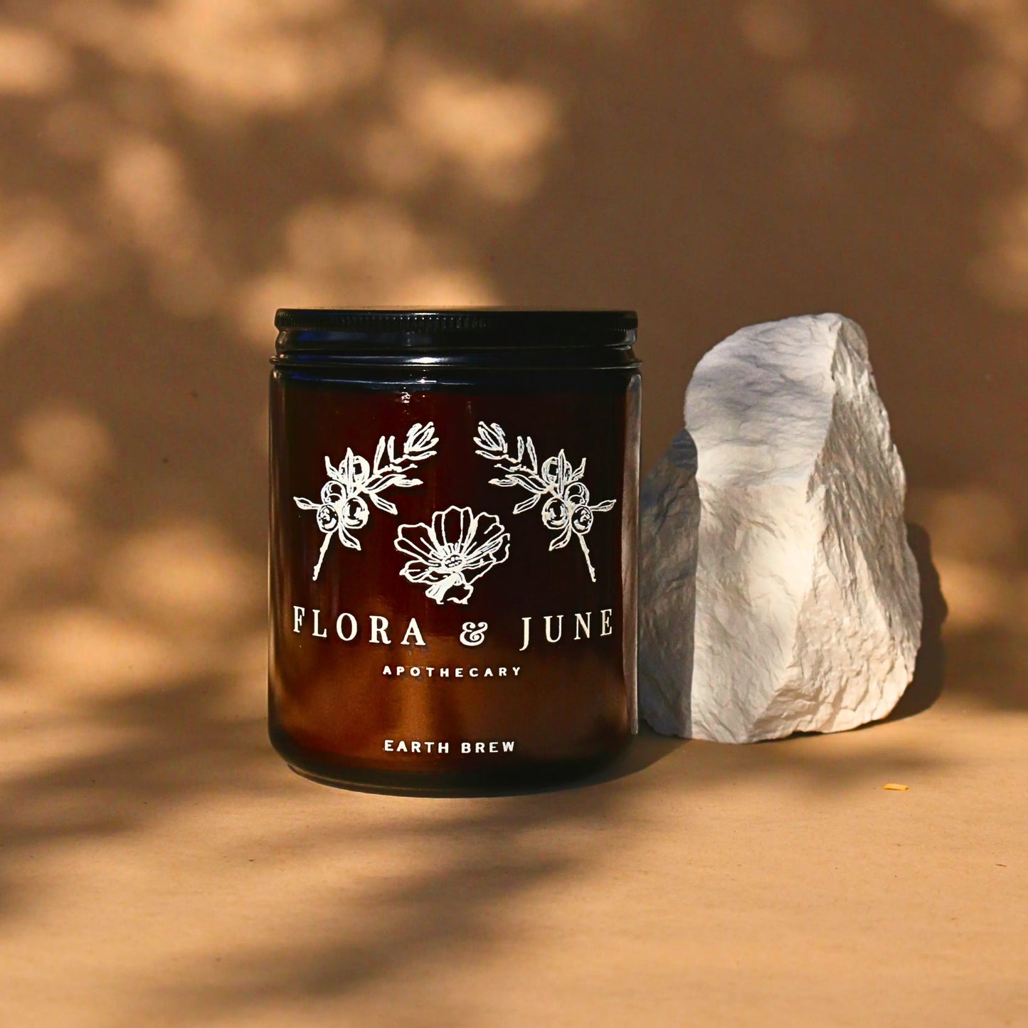Elegantly presented Flora & June Apothecary Earth Brew in an amber jar alongside a white stone, resting on a natural surface with the play of light and shadow enhancing the premium organic herbal blend.