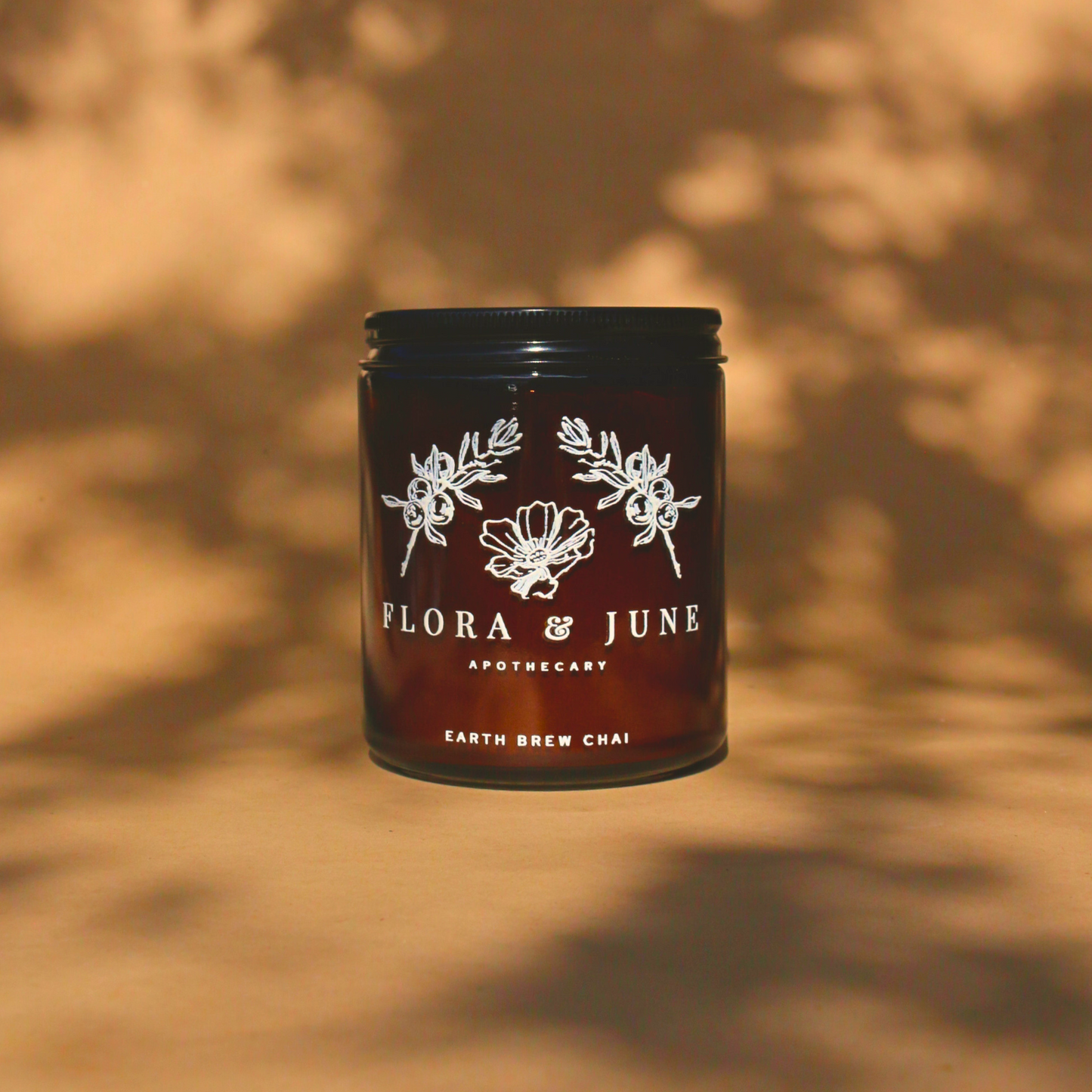 Flora & June Apothecary's Earth Brew Chai in a sleek, dark jar with intricate white botanical illustrations, presented on a textured backdrop with a pattern of natural shadows, symbolizing an organic and energising chai blend.