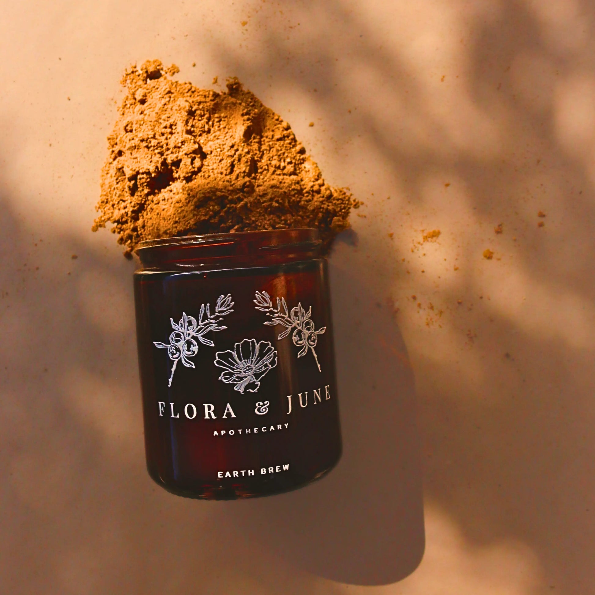 Flora & June's Earth Brew mushroom blend overflows from an amber jar against a backdrop of soft shadows and warm light, invoking the organic vitality of the morning ritual replacement for coffee.