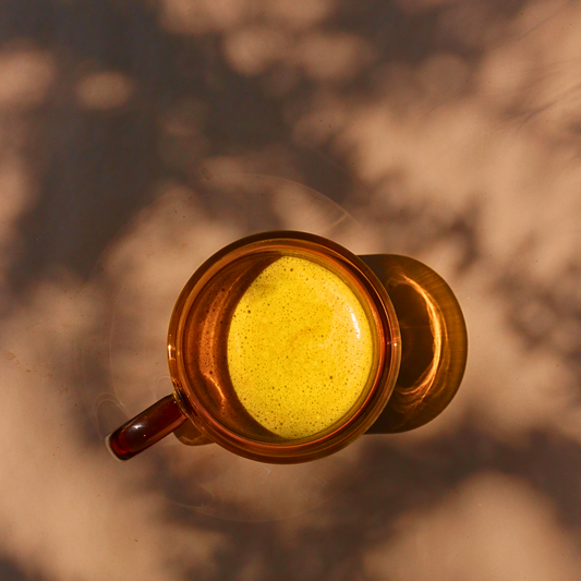 An amber glass mug, basking in the dappled morning light, filled with the vibrant Liquid Gold Latte.